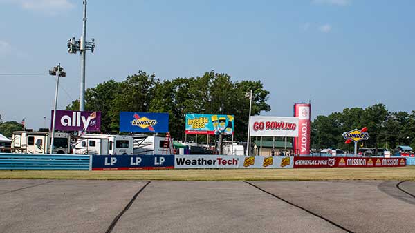 Trackside view at Watkins Glen International showing safety barriers and multiple sponsor signs, including Ally, Sunoco, Toyota, WeatherTech, and Go Bowling.
