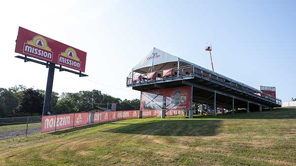 Elevated hospitality structure and viewing deck at Watkins Glen International, branded with Mission signage, overlooking a grassy hillside near the track.